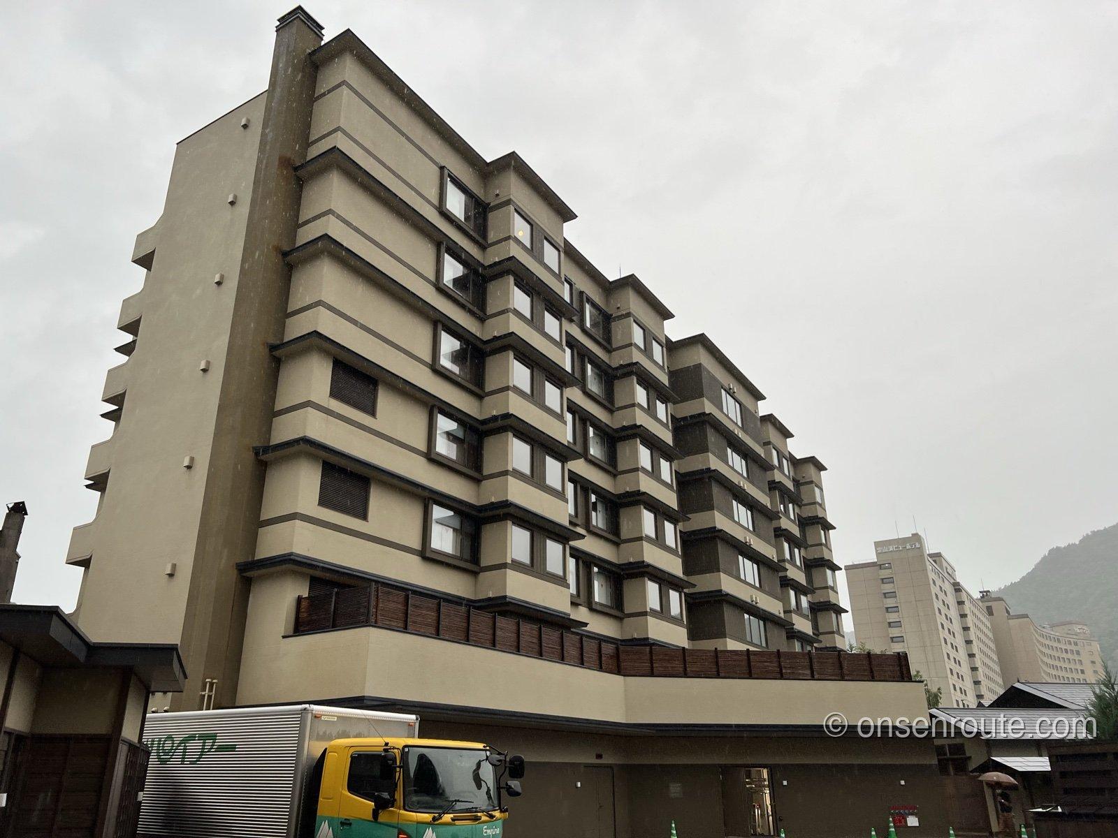 定山渓 ゆらく草庵の外観。曇り空の下、バルコニーが連なる7階建ての建物を見上げる