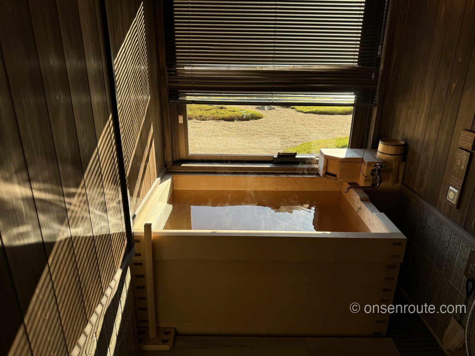 朝の光が差し込む客室の温泉風呂。満たされた湯面に窓からの光が反射している