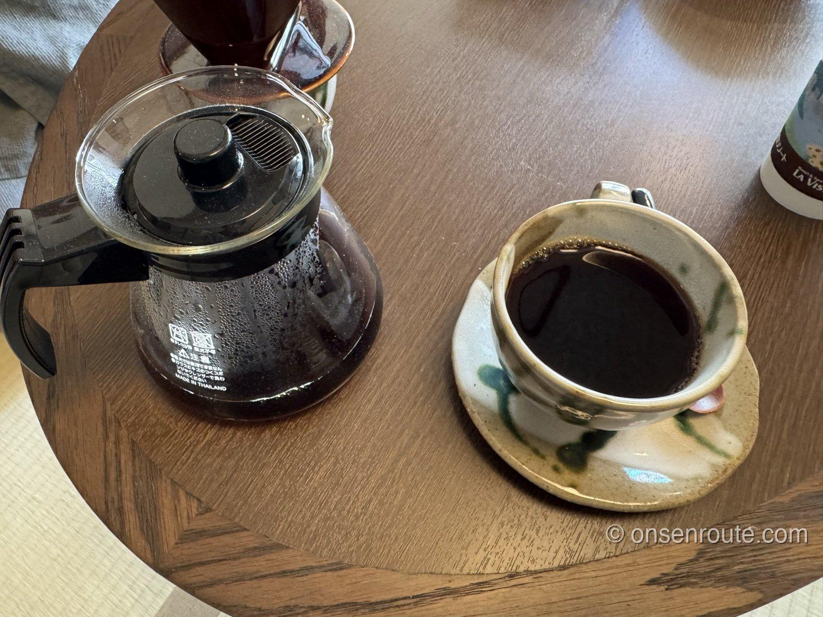 丸い木のテーブルに置かれたコーヒーサーバーと、陶器のカップに注がれたコーヒー