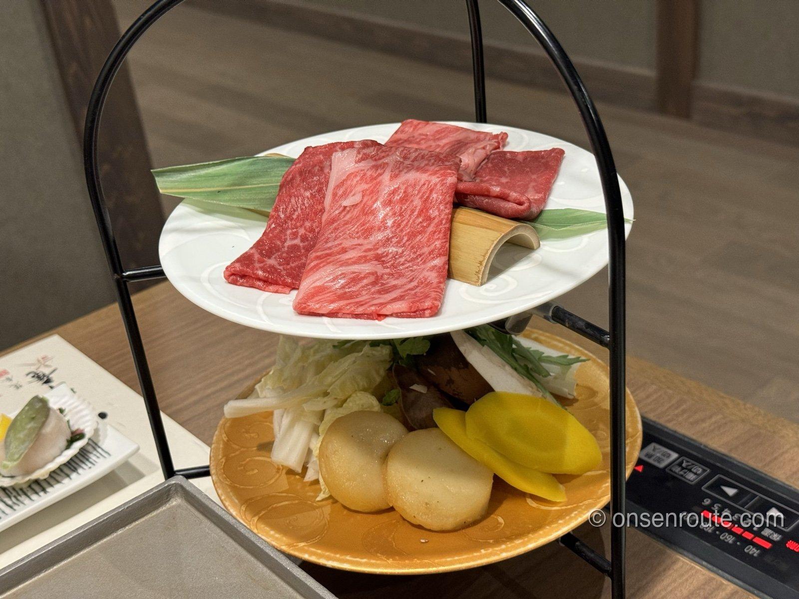 二段の台の上段に、サシの入った牛肉のスライスが笹の葉とともに盛られている。下段には野菜と麩