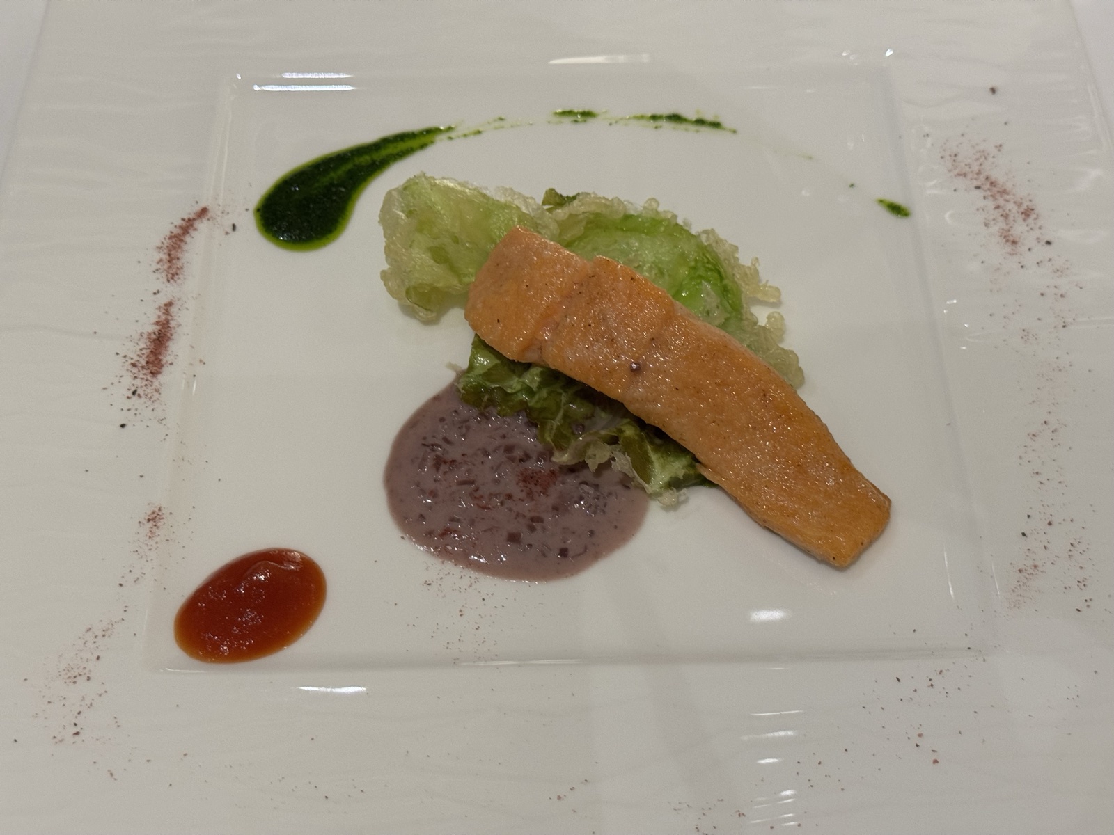 ホリホックのコースの魚料理。ソースとハーブオイルで彩られた白い角皿