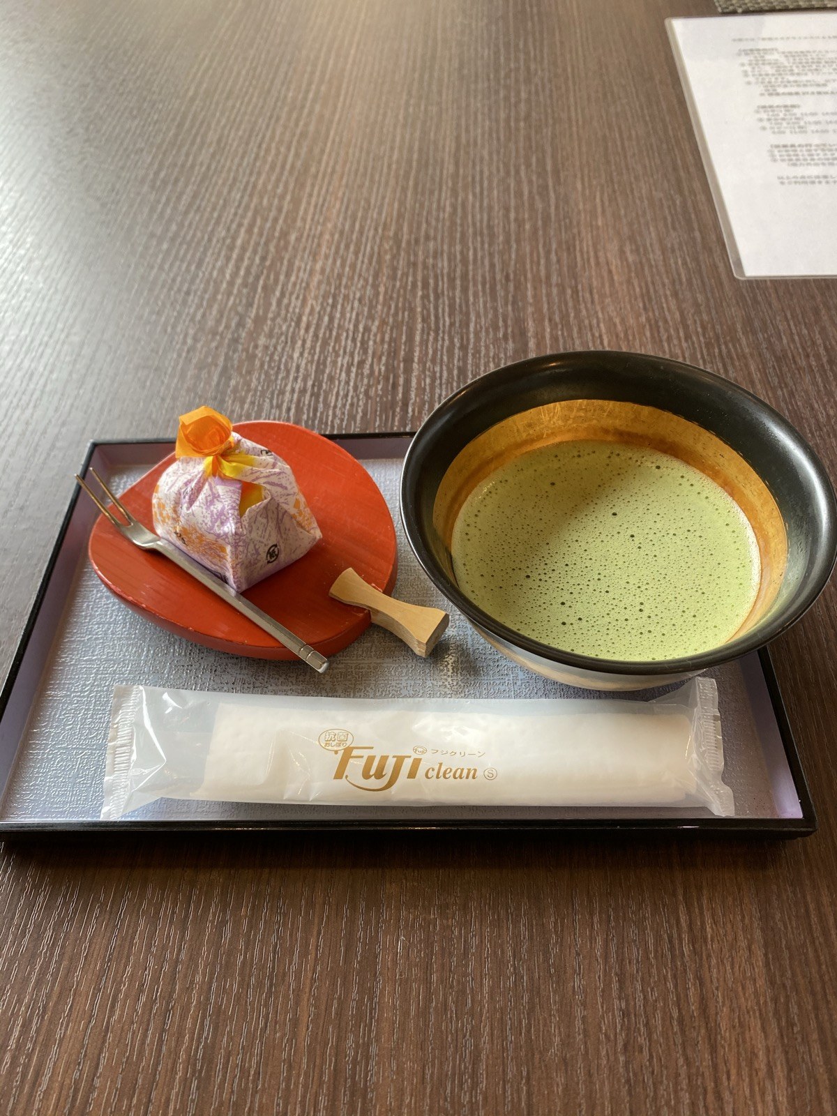 黒い茶碗に点てられた抹茶と、赤い皿にのった包み菓子。黒いお盆にのっている