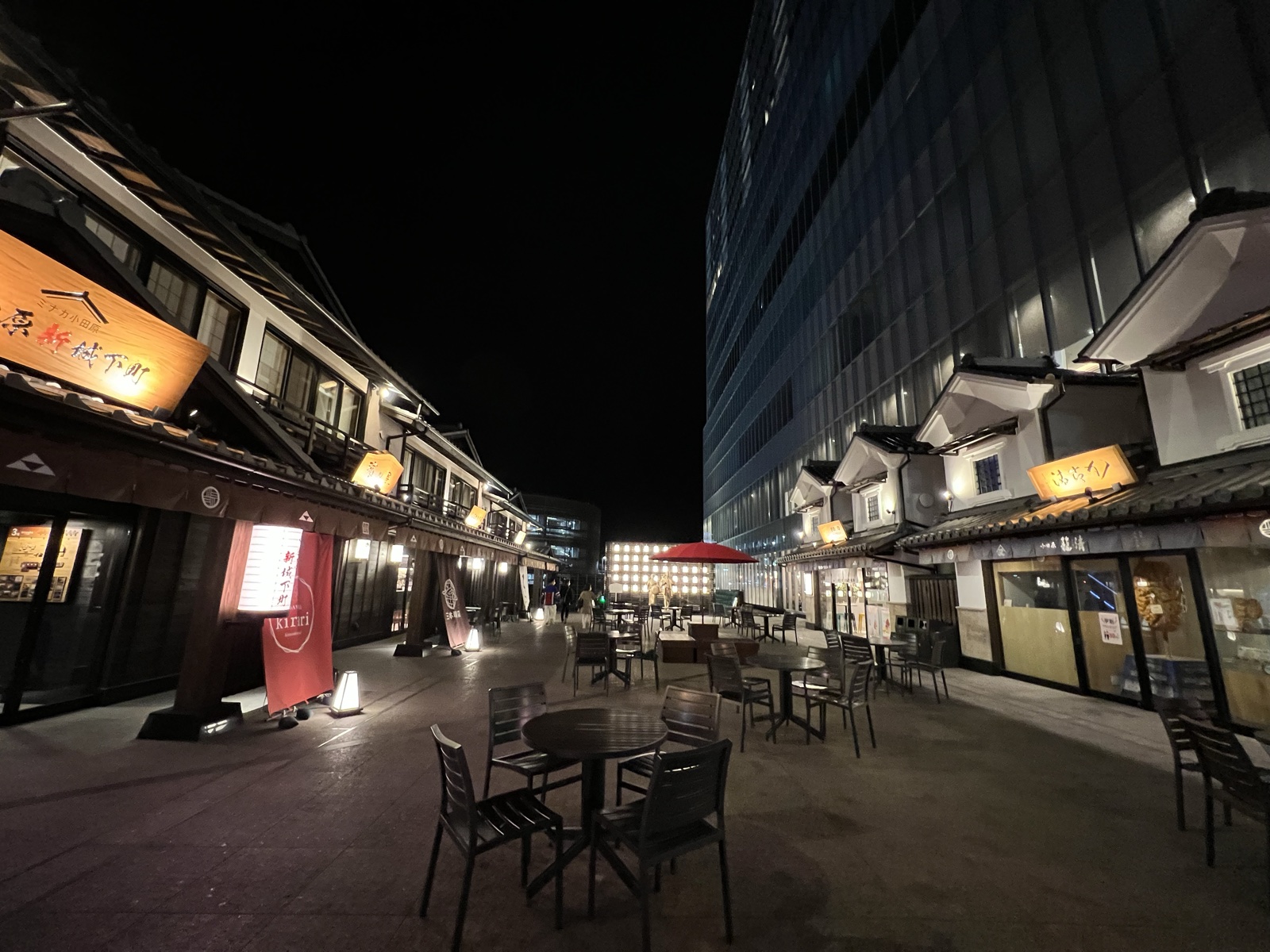 ミナカ小田原の江戸風の街並み「金次郎広場」の夜景。提灯の灯る木造の建物の奥にタワー棟がそびえる