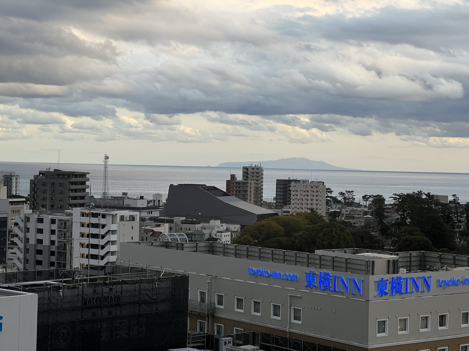 部屋の窓から見た小田原の街並みと相模湾。水平線に伊豆大島のシルエットが浮かぶ